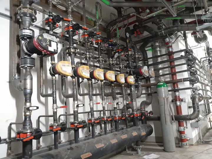 Rozdělovač s řadou měřičů, ventilů a potrubí pod stropem