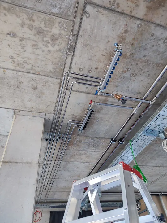 Nové rozvody s rozdělovačem pod betonovým stropem, pod nimi štafle